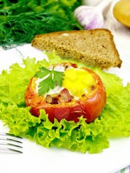 Scrambled eggs with ham and mushrooms in a tomato on a green lettuce in the plate, bread, fork on the background light wooden boards