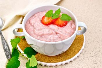 Strawberry soup with berries and mint in a bowl on a stand, towel on a background of a granite table