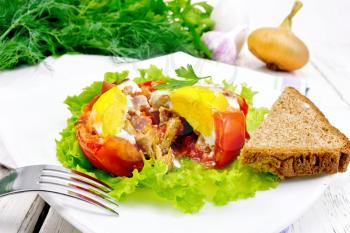 Scrambled eggs with ham and mushrooms in a tomato on a green lettuce in the plate, bread, fork on the background of wooden boards