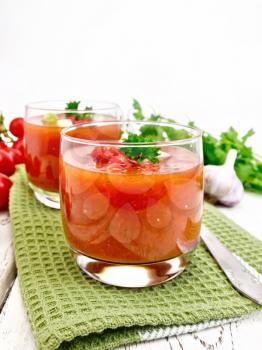 Gazpacho tomato soup in two glasses with parsley and vegetables on the green napkin on the background light wooden boards
