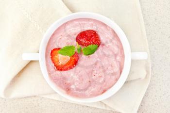 Strawberry soup with berries and mint in a bowl on a towel on the background of a granite table top