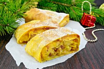 Strudel pumpkin and apple with raisins on parchment, pine branches with Christmas toys in the background of a wooden board