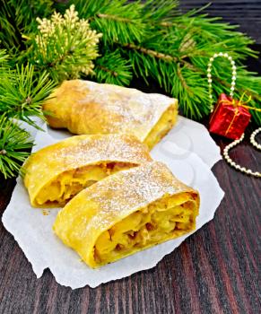 Strudel pumpkin and apple with raisins on paper, pine branches with Christmas toys in the background of a wooden board