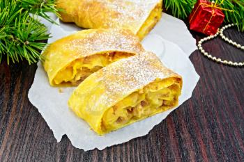 Strudel pumpkin and apple with raisins on parchment, pine branches with Christmas toys on a dark wooden board