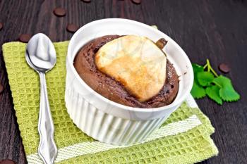 Cake with chocolate and pear in a white bowl, spoon on a napkin, mint on the background of wooden boards