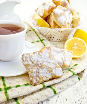 Cookies lemon, tea in a white cup on saucer on a napkin, lemons on a background of wooden boards