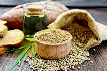 Hemp flour in a bowl, seed in a bag on the table, oil in a glass jar,  cannabis leaf and bread on a wooden boards background