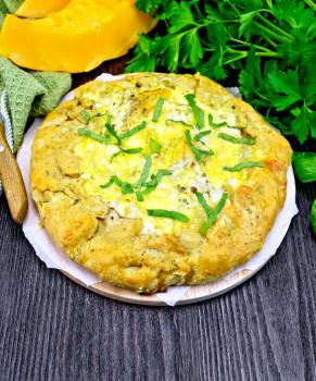 Pie of pumpkin, salty feta cheese, egg, cream and herbs, napkin, basil and parsley on a background of wooden boards