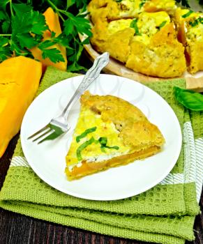 One piece of the pie of pumpkin, salty feta cheese, eggs, cream and herbs in a plate on towel, basil on a wooden boards background
