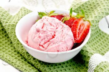 Ice cream strawberry in a white bowl with berries on a green napkin on a wooden board background