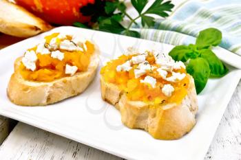 Bruschetta with pumpkin, salted feta cheese in a plate, garlic, basil and parsley, napkin and vegetable on a wooden board background