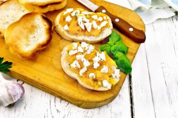 Bruschetta with pumpkin, salted feta cheese, garlic and basil, towel, knife and orange vegetable on a light wooden board background
