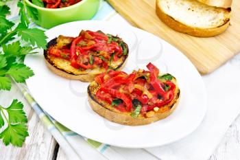 Bruschetta with roasted tomatoes, peppers, garlic, onions and parsley in a plate on a napkin on the background light wooden boards