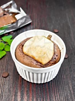 Cake with chocolate and pear in a white bowl, mint on the background of dark wood planks