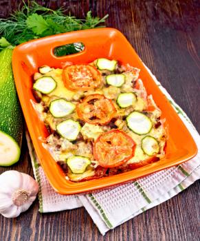 Baked minced meat, tomatoes and zucchini in a brazier on a napkin on the background of a dark wooden board