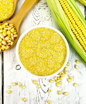 Corn grits in a bowl and spoon, cobs and grains on the background of the wooden planks on top