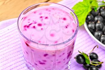 Milk cocktail with black currant in a glassful on a towel, saucer with berries on a wooden board background