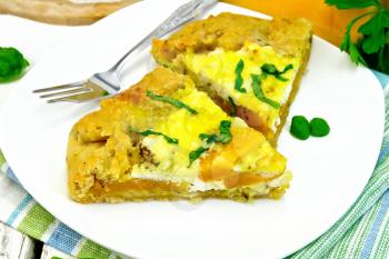 Two piece of the pie of pumpkin, salty feta cheese, eggs, cream and herbs in a plate on towel, basil on a wooden boards background