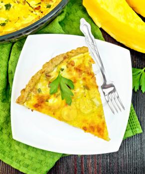 Piece of pie kish with pumpkin and bacon, filled with milk with eggs and cheese in a plate on a napkin, parsley on a wooden board background from above