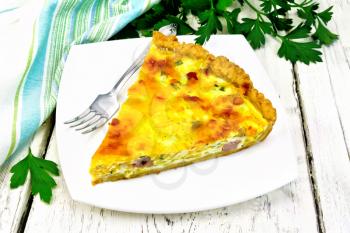 Piece of pie kish with pumpkin and bacon, filled with milk with eggs and cheese in a plate, parsley, napkin on a wooden board background