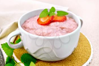 Strawberry soup with berries and mint in a bowl on a stand, a napkin and a spoon on a background of a granite table