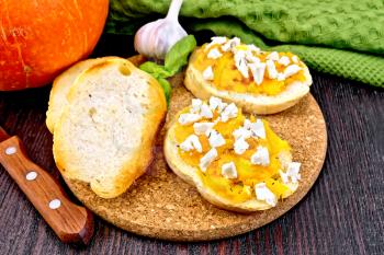 Bruschetta with pumpkin, salted feta cheese, garlic and basil, napkin, knife and orange vegetable on a wooden board background