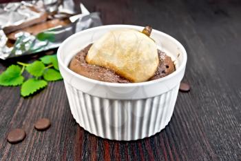 Cake with chocolate and pear in a white bowl, mint on the background of dark wood planks