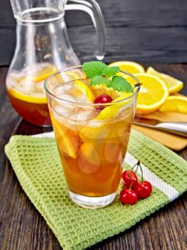 Lemonade in a glassful and jug with a cherry, lemon, orange and mint on a green towel, a board with fruits on a wooden board background
