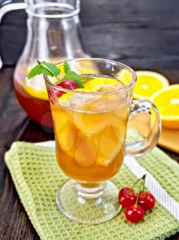 Lemonade in a wineglass and jug with a cherry, lemon and orange, mint on a napkin on a background of a dark wooden board