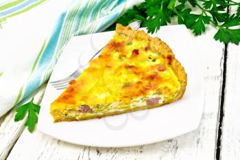 Piece of pie kish with pumpkin and bacon, filled with milk with eggs and cheese in a plate, parsley, napkin on a background of light wooden board