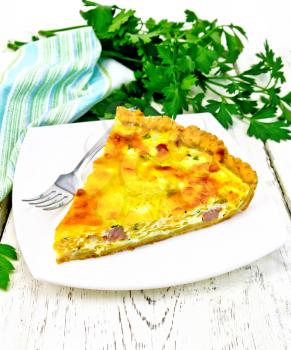 Piece of pie kish with pumpkin and bacon, filled with milk with eggs and cheese in a plate, parsley, towel on wooden plank background
