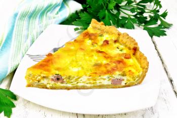 Piece of pie kish with pumpkin and bacon, filled with milk with eggs and cheese in a plate, parsley, a towel on the background of a light wooden board