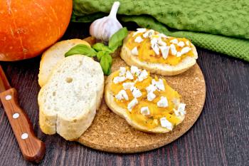 Bruschetta with pumpkin, salted feta cheese, garlic and basil, green napkin, knife and orange vegetable on a wooden board background