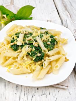 Penne pasta with spinach and cedar nuts in a plate on a napkin on a wooden board background
