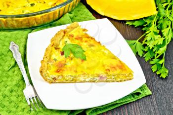 Piece of pie kish with pumpkin and bacon, filled with milk with eggs and cheese in a plate on a green napkin, parsley on a wooden plank background