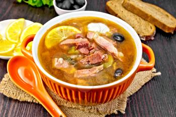 Soup saltwort with lemon, meat, pickles, tomato sauce olives in a bowl on a sacking, bread on a wooden board background