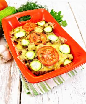 Casserole from minced meat, tomatoes and zucchini in a brazier on a napkin on a light wooden board background