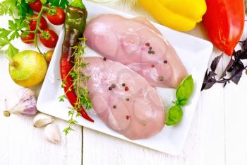 Chicken breast with hot pepper and thyme in a white plate, napkin, parsley and basil, onion, garlic and vegetables on a wooden plank background