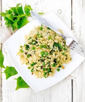 Couscous with spinach and green peas in a plate on a towel, basil and fork on a wooden plank background