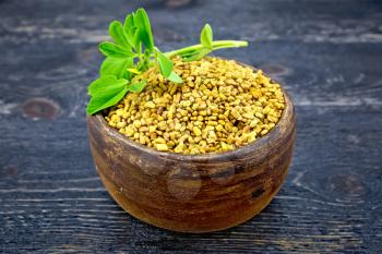 Fenugreek in a clay bowl with green leaves on a wooden plank background