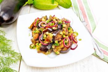 Salad of fried eggplant, fresh and pickled cucumber with red onion, seasoned with vegetable oil and spicy sauce in a plate, napkin, fork and dill on a light wooden board background