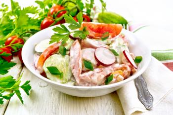 Salad of fresh tomatoes, cucumbers and radish with green onions and parsley,  flavored with mayonnaise and sour cream in a bowl, towel and fork on a wooden plank background
