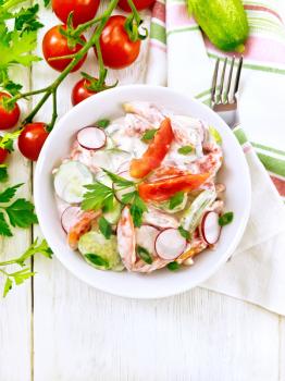 Salad of fresh tomatoes, cucumbers and radish with green onions and parsley,  flavored with mayonnaise and sour cream in a bowl, towel and fork on the background of a light wooden board on top