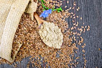 Flaxseed flour in a spoon, seeds in a bag and on a table, blue linen flower on a background of a wooden board on top