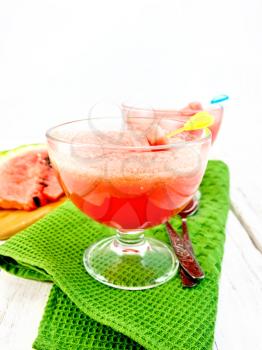 Jelly airy watermelon in two glass bowls, spoon on a green towel against a light wooden board