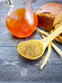 Malt in a spoon, bread, kvass in a glass jug and spikelets on the background of wooden board