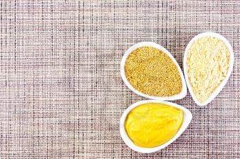 Mustard sauce, seeds and mustard powder in three saucepans on a background of brown woven napkin on top