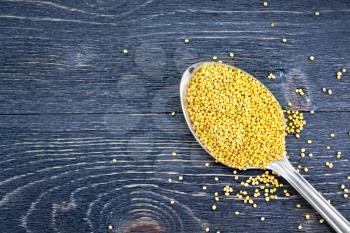 Mustard seeds in a metal spoon on the background of a wooden board from above