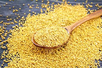 Mustard seeds in a spoon and on a table on the background of a black wooden board
