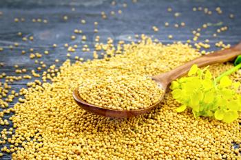 Mustard seeds in a spoon and on a table with a flower on wooden board background